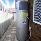 Heat pump in Australia system is installed outside next to a brick wall and a window with a security screen.